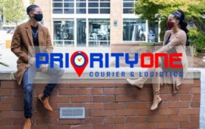 Two people sitting on a brick wall with the priority one logo in front of them.